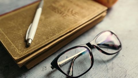 A notebook, pen and reading glasses on a wooden desk