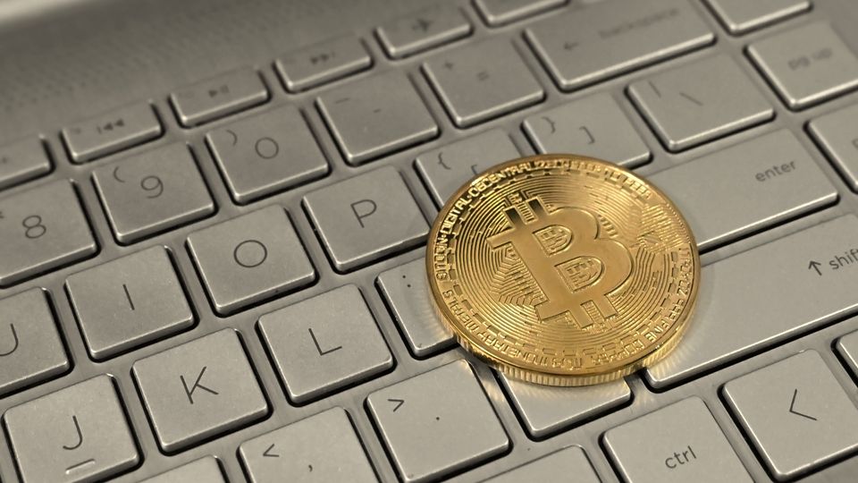 A gold-coloured physical bitcoin souvenir coin on a laptop keyboard