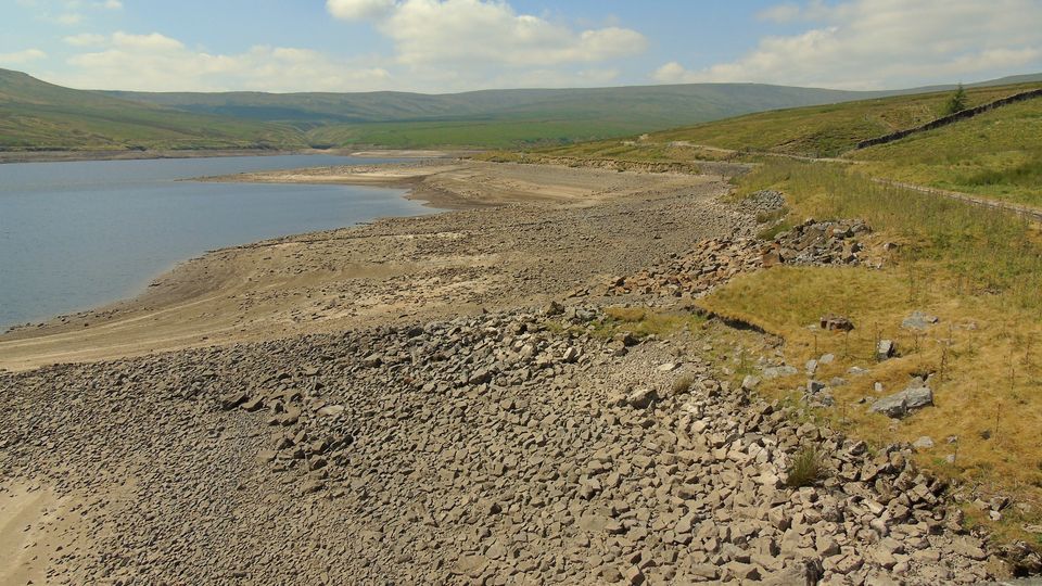 A reservoir with low water exposing its dry, stony shore